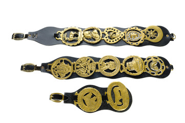 Antique horse brasses attached to leather straps used as decoration on horses that pulled carts in the late 19th and early 20 centuries, isolated on white