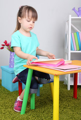 Little girl reads book sitting at table in room