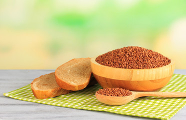 Composition with raw buckwheat in bowl, spoon and fresh bread