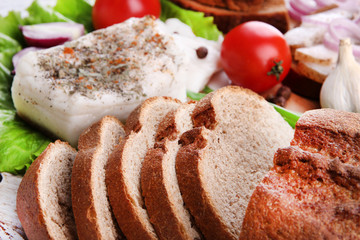 Slices of bread and lard with vegetables on table close up