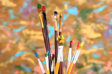 Fototapeta premium Many brushes in paints on multicolor wooden background