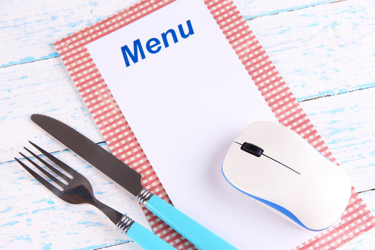 Computer mouse with menu and cutlery on wooden background