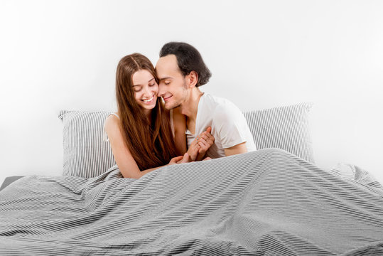Happy couple in bed smiling and flirting with one another on whi