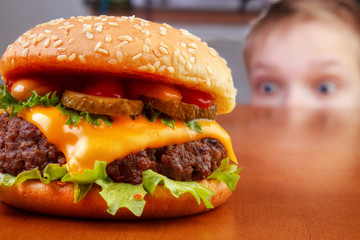 Hungry young boy is staring beef burger on table