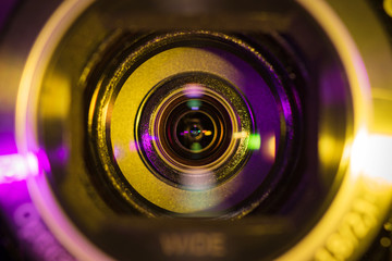 Video camera lens closeup lit by yellow and purple neon light