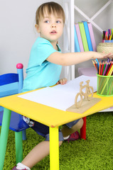 Little girl draws sitting at table in room