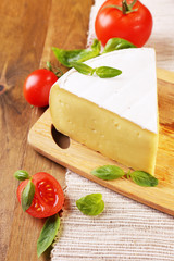 Tasty Camembert cheese with tomatoes and basil, on wooden table