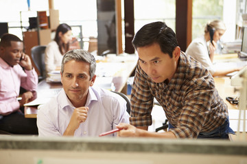 Fototapeta premium Two Colleagues Working At Desk With Meeting In Background