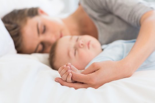 Mother sleeping with baby son on bed