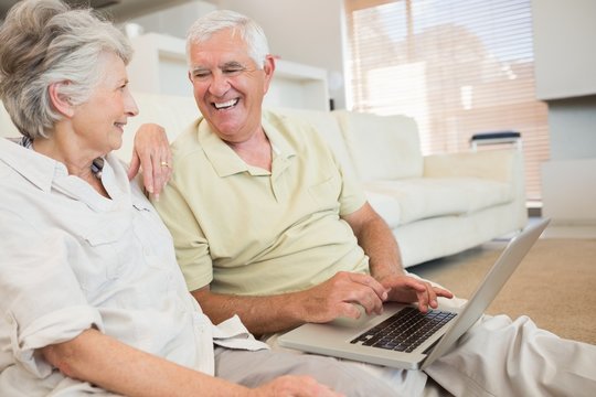 Cheerful senior couple using the laptop together sitting on rug