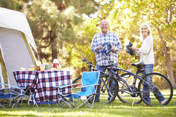 Senior Couple Riding Bikes On Camping Holiday In Countryside