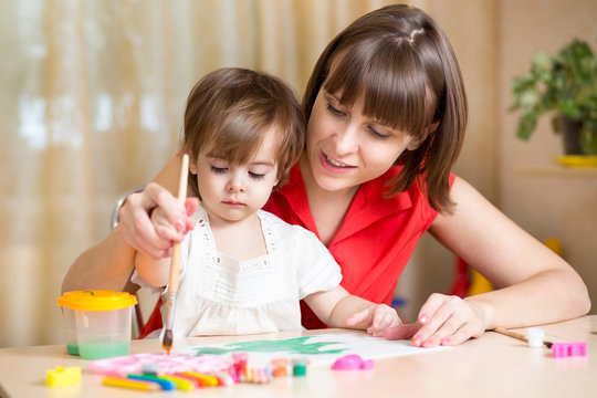 mom and kid girl paint together at home