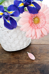 Blue irisis and pink gerbera daisy flower in white basket