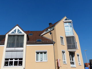 Modernes Eckhaus mit spitzen Giebeln und modernen Fenstern mit Sonnenschutz bei blauem Himmel und...