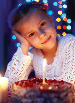 Cute little girl looking at cake with a candle