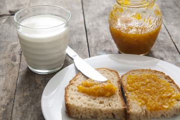 Bread with orange jam and glass of milk on wooden table