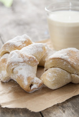 Milk and sweet rolls with sugar on a wooden background