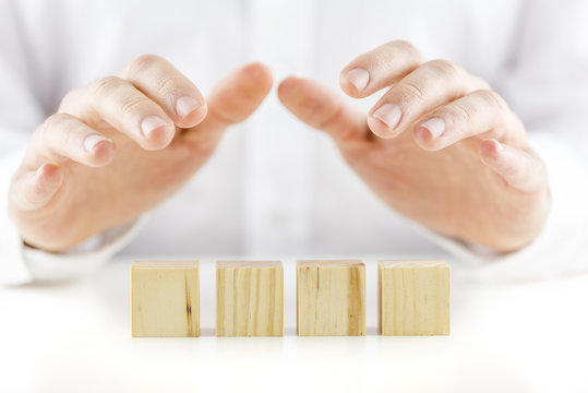Man holding his hands protectively over a row of four blank cube
