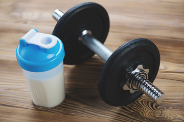 Shaker with protein and a dumbbell on a wooden surface, close-up