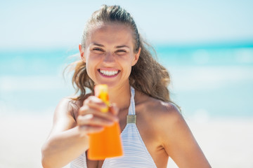 Smiling young woman pointing bottle of sun block creme in camera