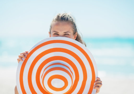 Young Woman Hiding Behind Hat On Beach