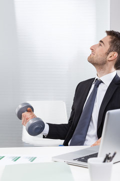 Young businessman holding dumbbell in office