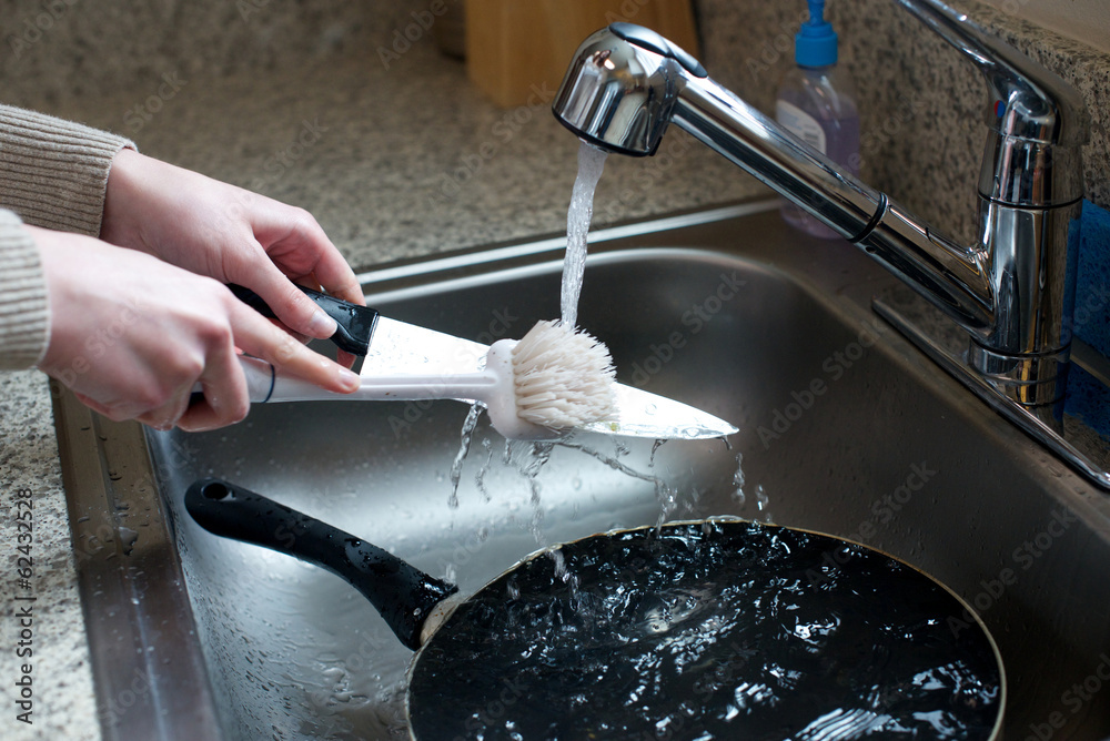 Wall mural close up of hands scrubbing knife in sink