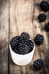 Fresh Blackberries in a white bowl on  wooden table closeup with