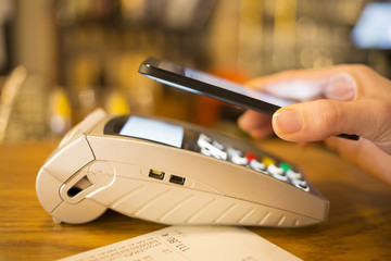 Woman paying with NFC technology on mobile phone, restaurant, sh