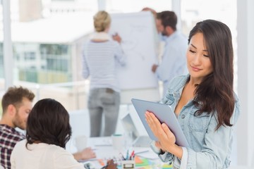 Fototapeta premium Asian woman using her tablet pc while her colleagues are working