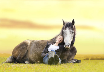 girl and gray Arabian horse lie at sunset on summer pasture