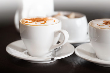 White cups of cappuccino stands on dark wooden table