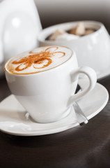 White cup of cappuccino stands on dark wooden table