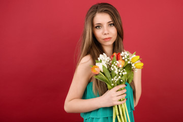Beautiful girl in a summer dress with tulips on a red background