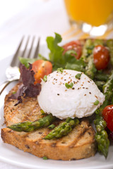 Poached egg on toasted bread with asparagus, tomatoes and greens