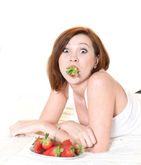 Young Attractive woman eating a bowl of strawberries in bed