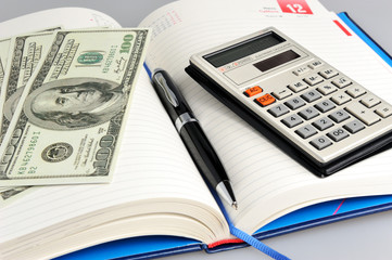 Dairy with black pen, calculator and money closeup