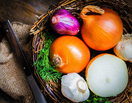 Colorful onions and garlic in the basket on rustic wooden backgr