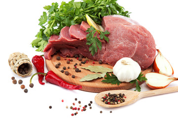 Raw meat, vegetables and spices on a wooden cutting board.
