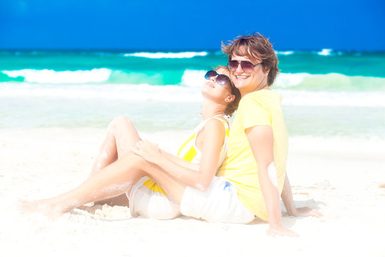 young happy couple in sunglasses sitting on tropical beach
