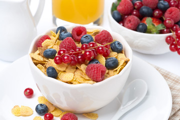 cornflakes with berries in a bowl, milk and orange juice