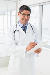 Smiling male doctor writing reports in hospital