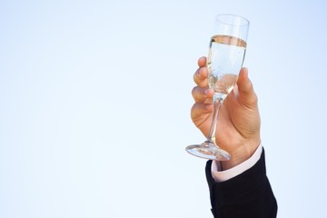 Hand raising champagne glass against clear sky