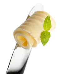 Curl of fresh butter with basil on knife, isolated on white