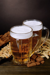 Glasses of beer with snack on table on dark background