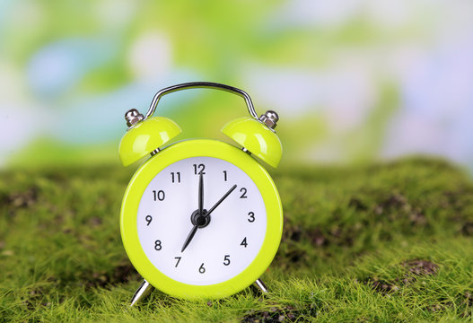 Green alarm clock on grass on natural background
