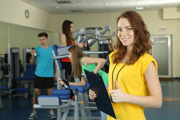 Young trainer and womans engaged in simulator in gym