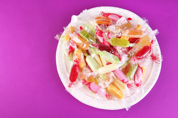 Tasty candies on plate on purple background