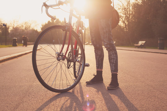 Young woman standing with bicycle at sunset