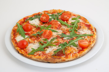 Pizza with tomato and arugula on white plate